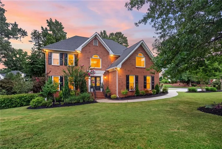 Traditional brick exterior featuring a dark shingle roof and black louvered shutters