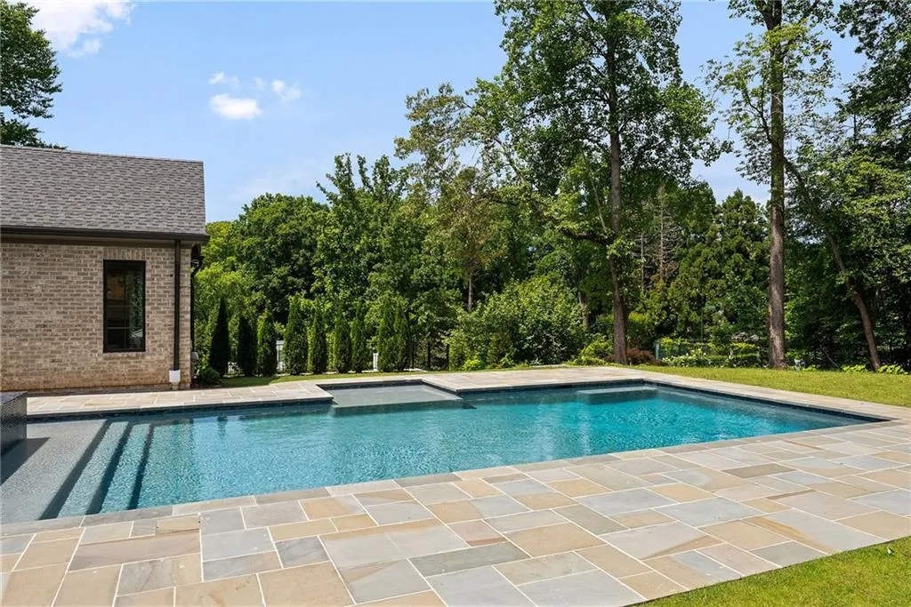 Expansive pool area featuring a rectangular swimming pool, integrated spa, and broad stone paver patio