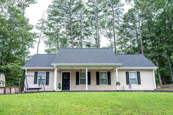 Ranch-style residence featuring a covered front porch with white columns, a dark shingled roof, and tan siding