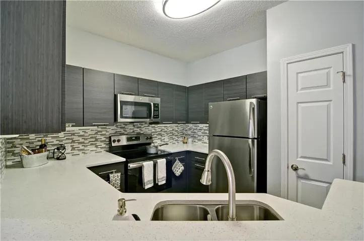 Kitchen featuring backsplash, light stone counters, appliances with stainless steel finishes, and sink