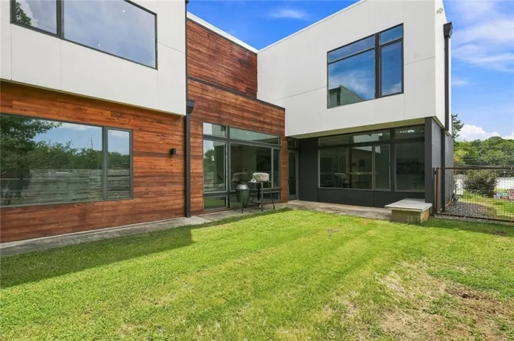 Modern exterior with white and wood-finish siding, large rectangular windows, and a grassy lawn