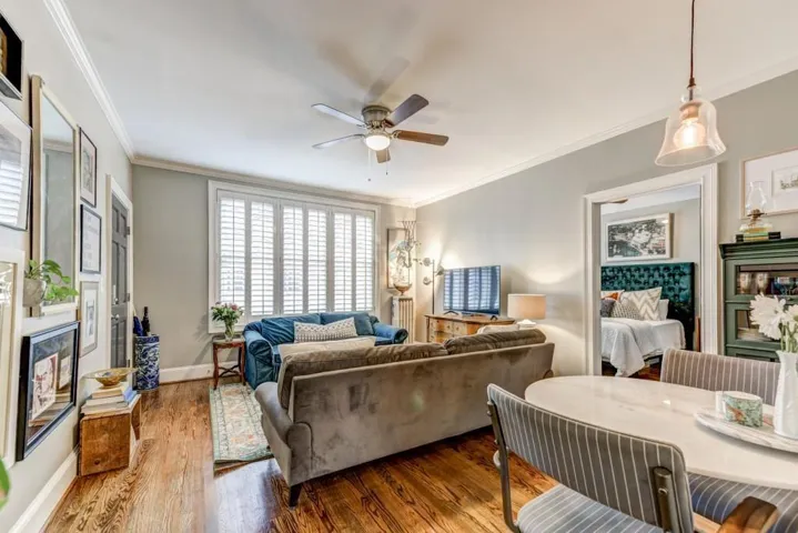 Living room with a fireplace, ornamental molding, wood-type flooring, a ceiling fan, and radiator