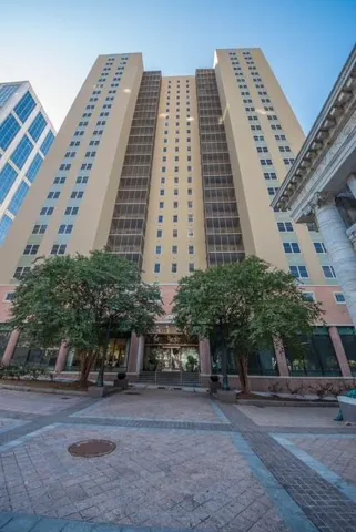High-rise building with a beige facade, ground-level commercial spaces, and a paver stone entrance