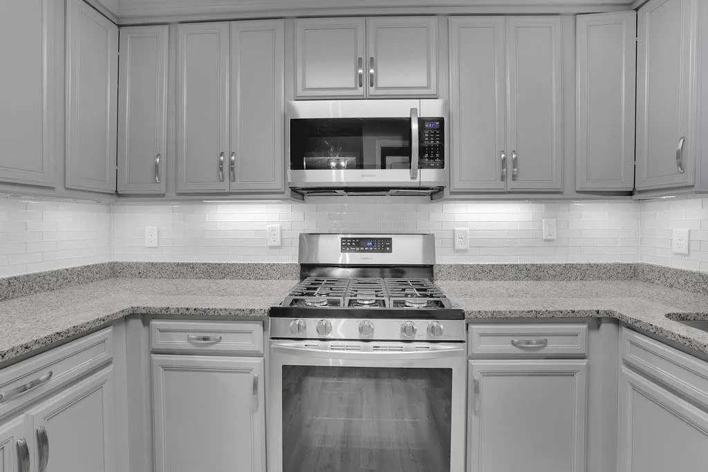 Kitchen with light stone counters, appliances with stainless steel finishes, gray cabinetry, and backsplash