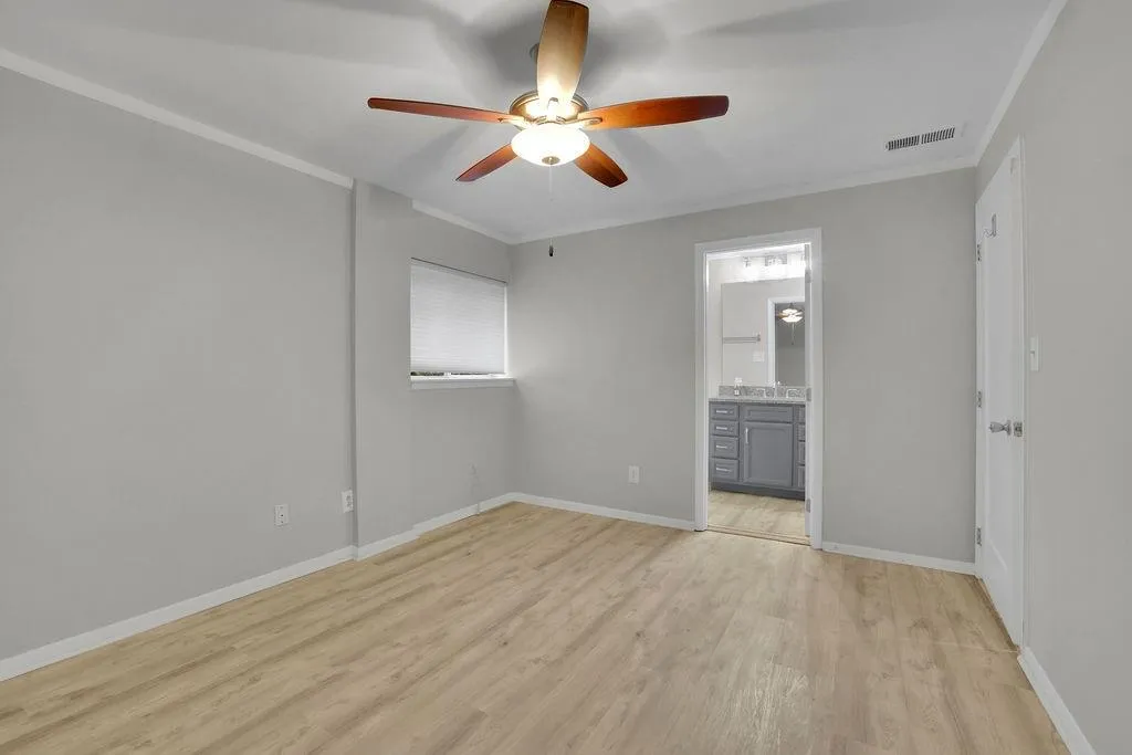 Unfurnished bedroom with ensuite bathroom, ornamental molding, light wood-type flooring, and ceiling fan