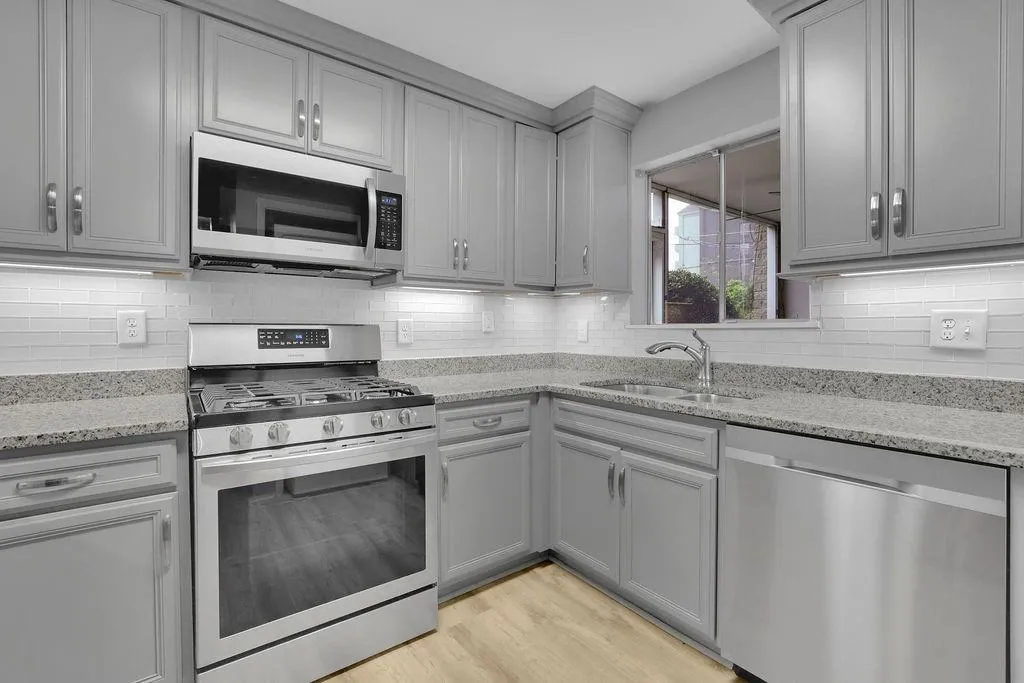 Kitchen with light stone counters, appliances with stainless steel finishes, light hardwood / wood-style flooring, and sink
