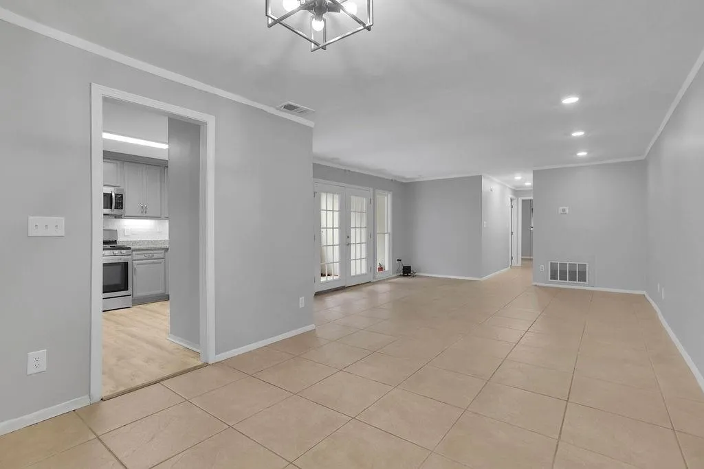 Spare room with french doors, crown molding, a notable chandelier, and light tile floors