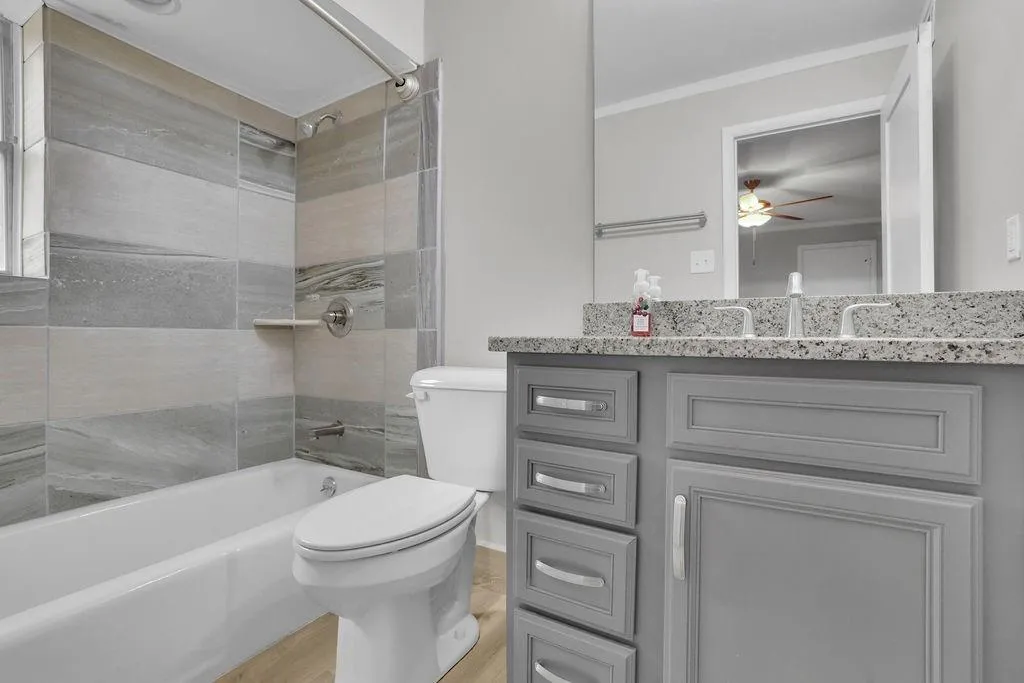 Full bathroom with wood-type flooring, vanity, tiled shower / bath, ceiling fan, and toilet