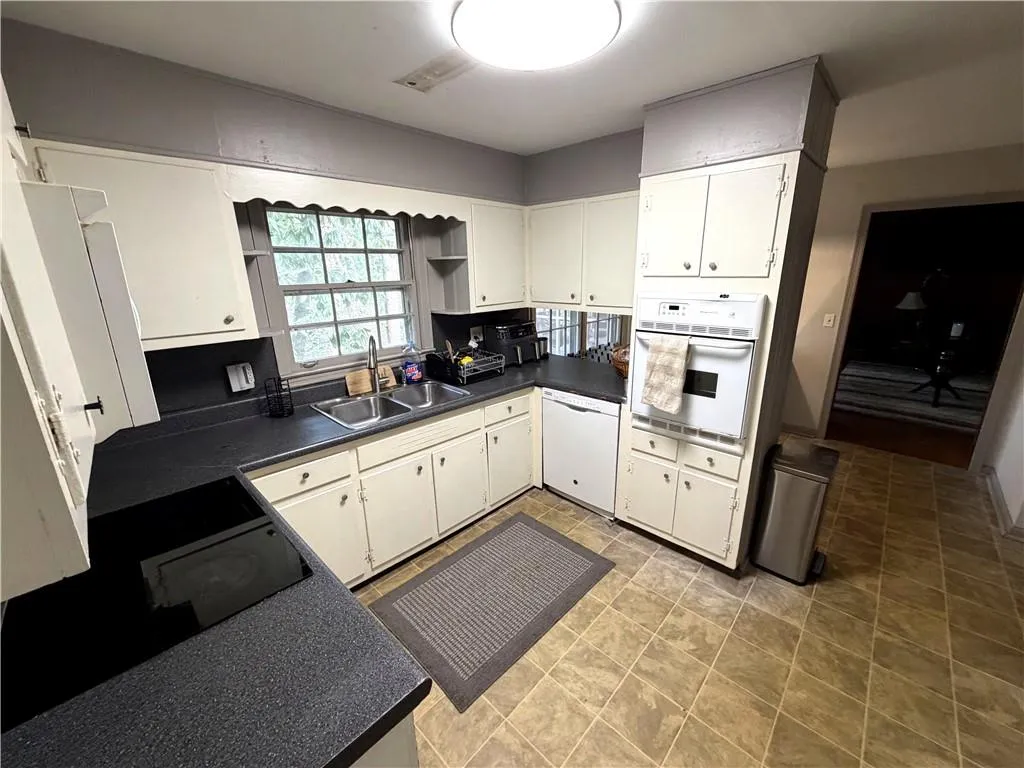 Kitchen with dark countertops, white appliances, and white cabinetry