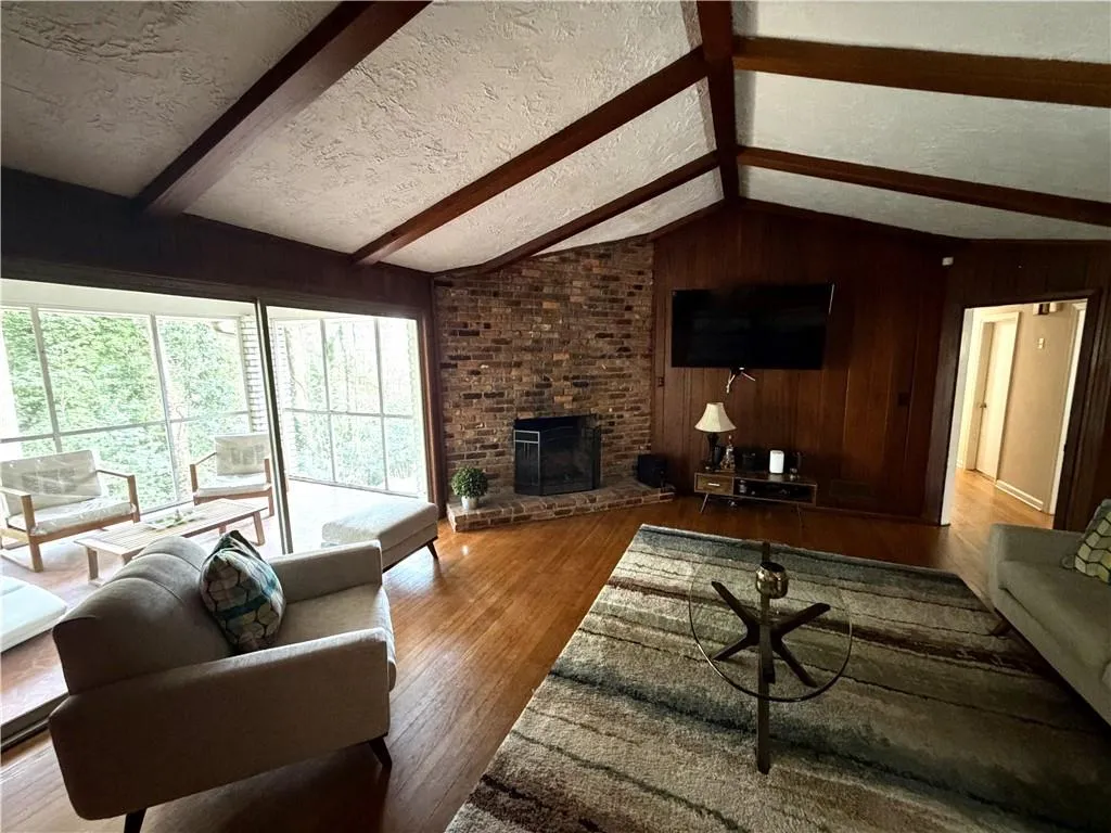 Living room featuring wooden walls, a textured ceiling, hardwood / wood-style floors, a fireplace, and beam ceiling