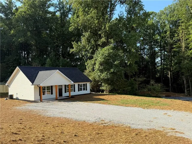 Modern ranch-style residence featuring white siding, a dark roof, and a gravel driveway
