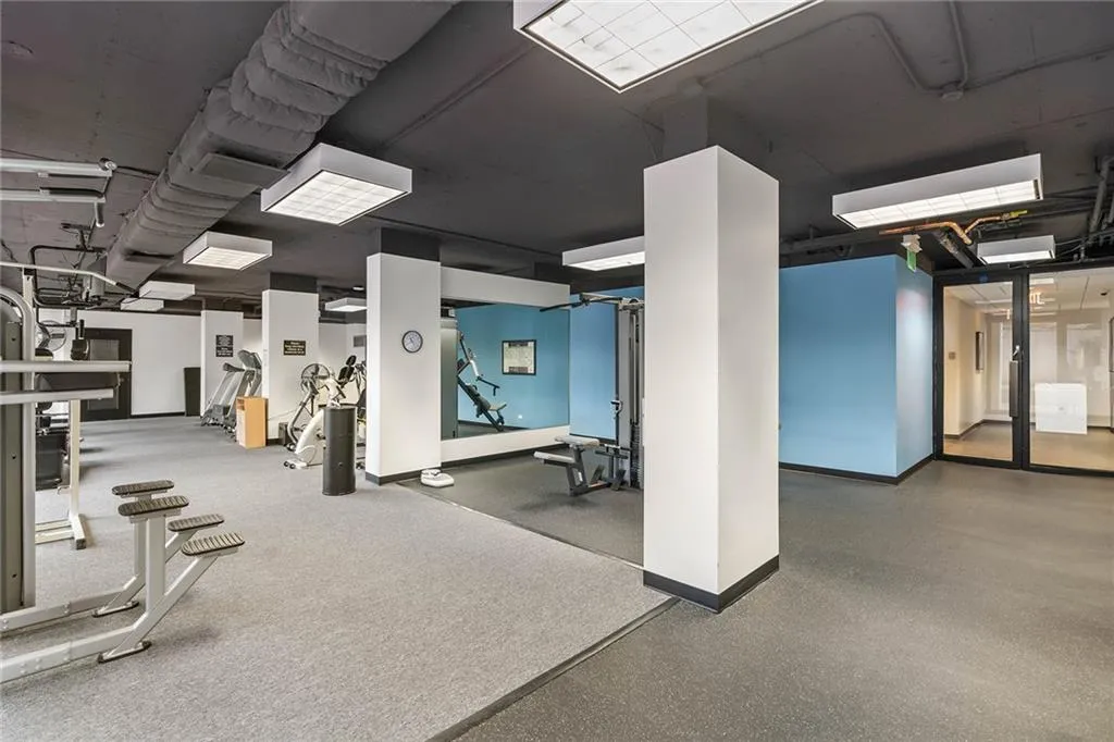 Fitness area featuring exposed ceiling architecture, rubberized flooring, large-scale wall mirrors, and recessed panel lighting