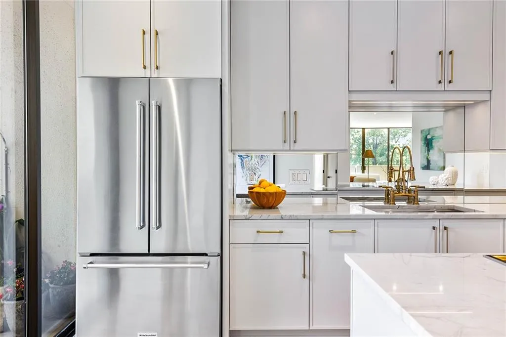 Kitchen featuring light-toned cabinetry, stone countertops, stainless steel French door refrigerator, mirror backsplash, and metallic hardware