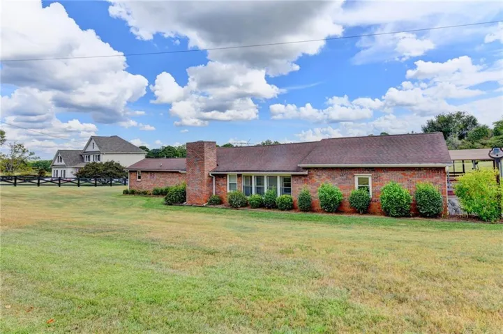 3 sided Brick exterior with a prominent brick chimney, classic shingle roof, and established landscaping.