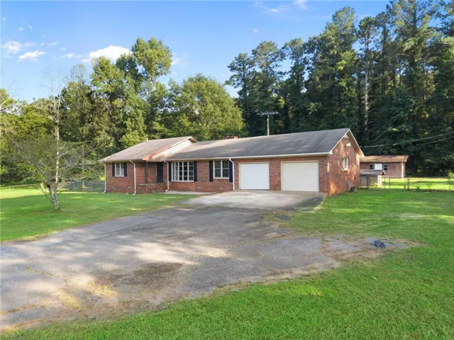 Brick exterior home featuring a two-car garage, mature trees, and an expansive front yard