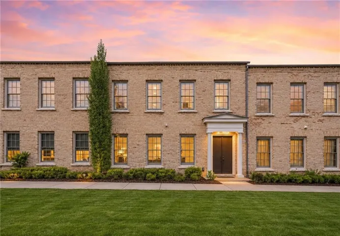 Brick exterior with multiple windows, a prominent covered entryway, manicured landscaping, and a verdant lawn