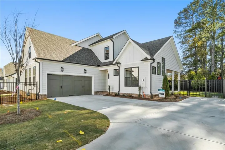Contemporary farmhouse exterior with white vertical and horizontal siding, dark-frame windows, a paved driveway, and a two-car garage with carriage-style doors