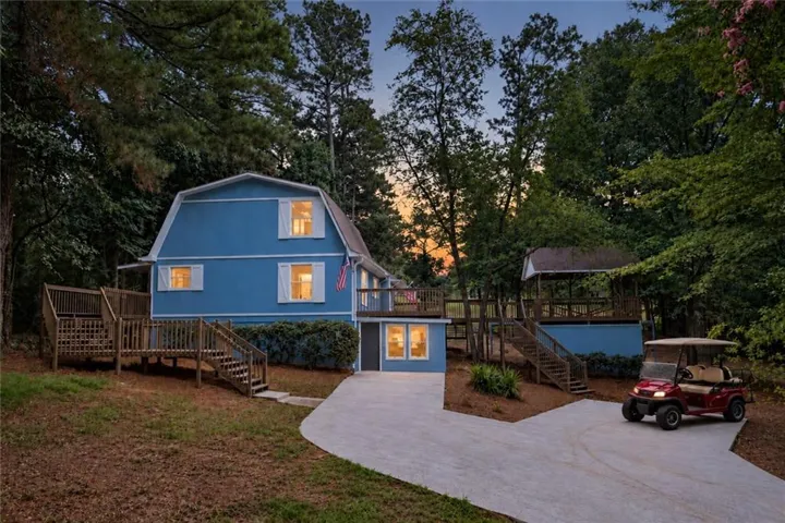 Gambrel-style exterior with blue siding, multiple outdoor decks, a detached covered structure, and a concrete driveway