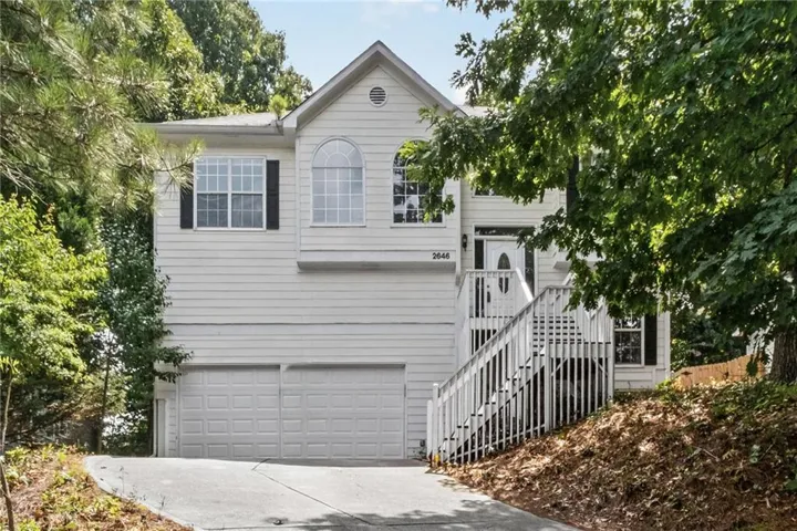 White split-level residence featuring a two-car garage, arched window, and prominent front entry staircase