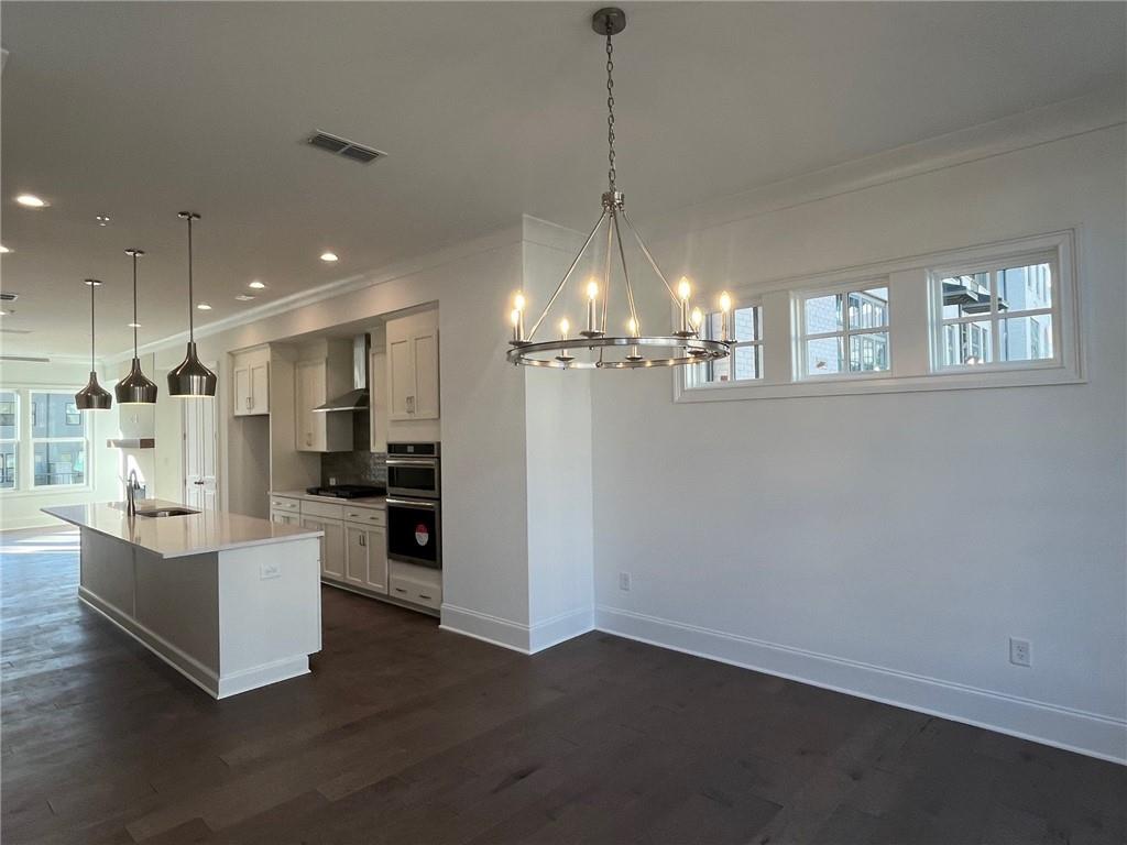 Kitchen featuring an island with sink, wall chimney range hood, dark hardwood / wood-style floors, and decorative light fixtures