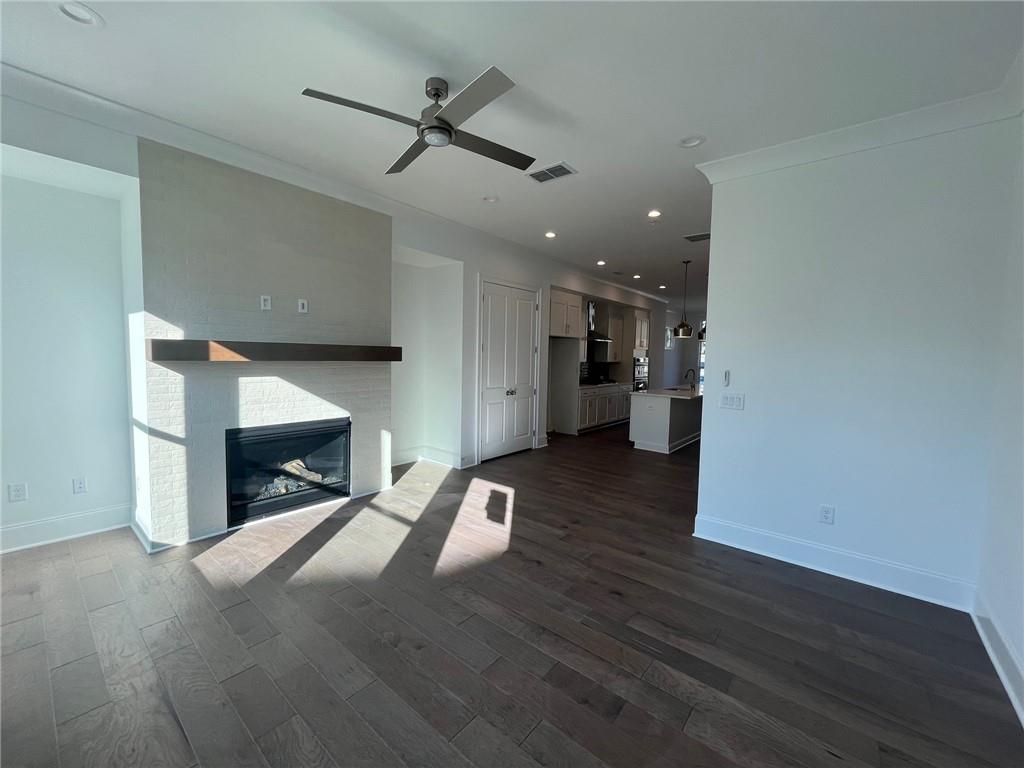 Unfurnished living room featuring dark wood-type flooring, crown molding, sink, and ceiling fan