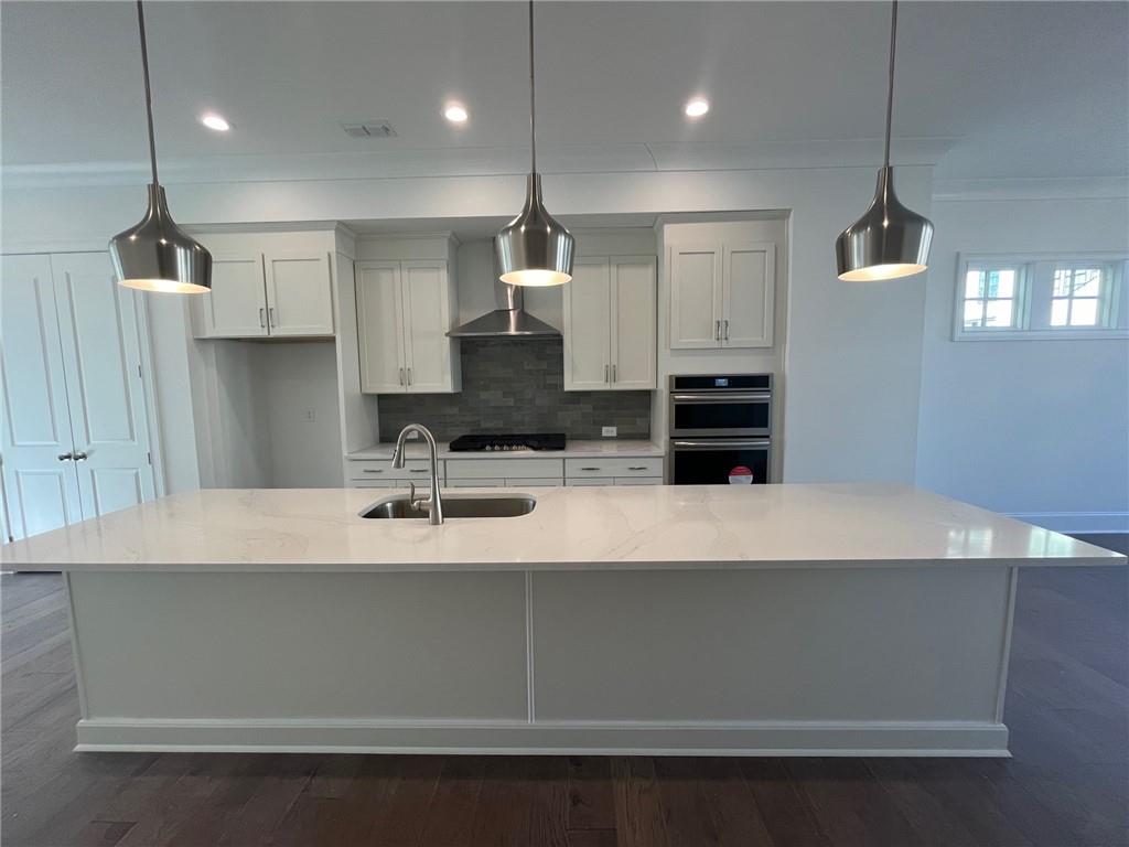 Kitchen with decorative light fixtures, appliances with stainless steel finishes, an island with sink, sink, and dark hardwood / wood-style floors