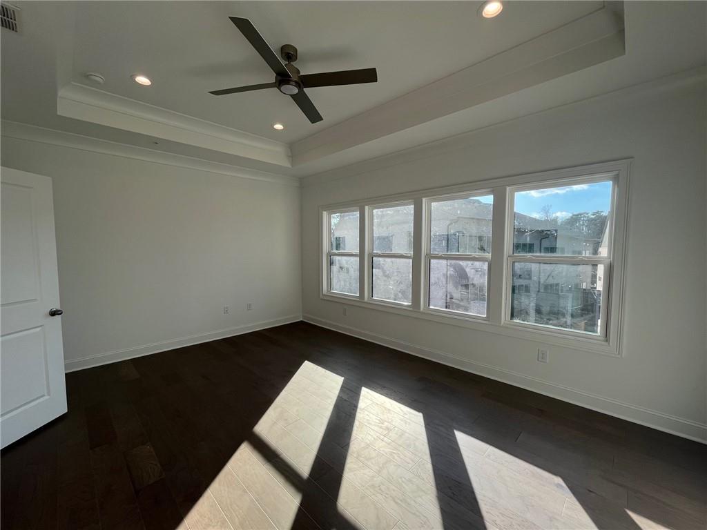 Empty room featuring dark hardwood / wood-style floors, a raised ceiling, and ceiling fan