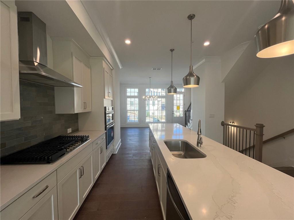 Kitchen featuring tasteful backsplash, white cabinetry, light stone countertops, decorative light fixtures, and wall chimney range hood