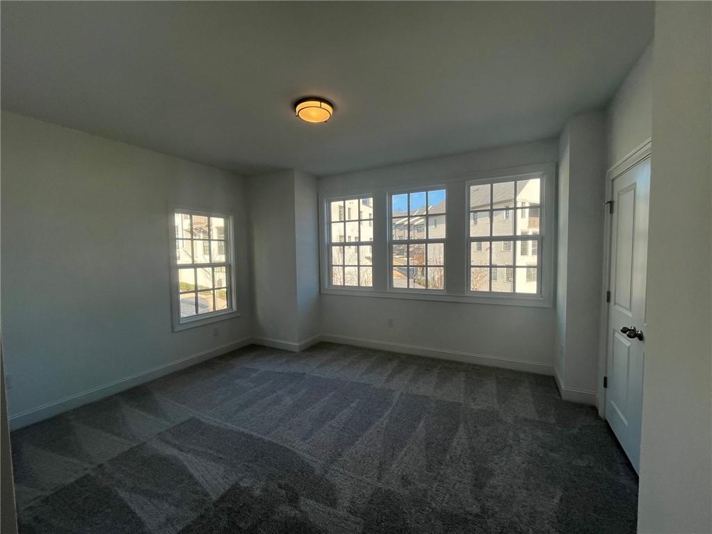 Unfurnished room featuring plenty of natural light and dark colored carpet