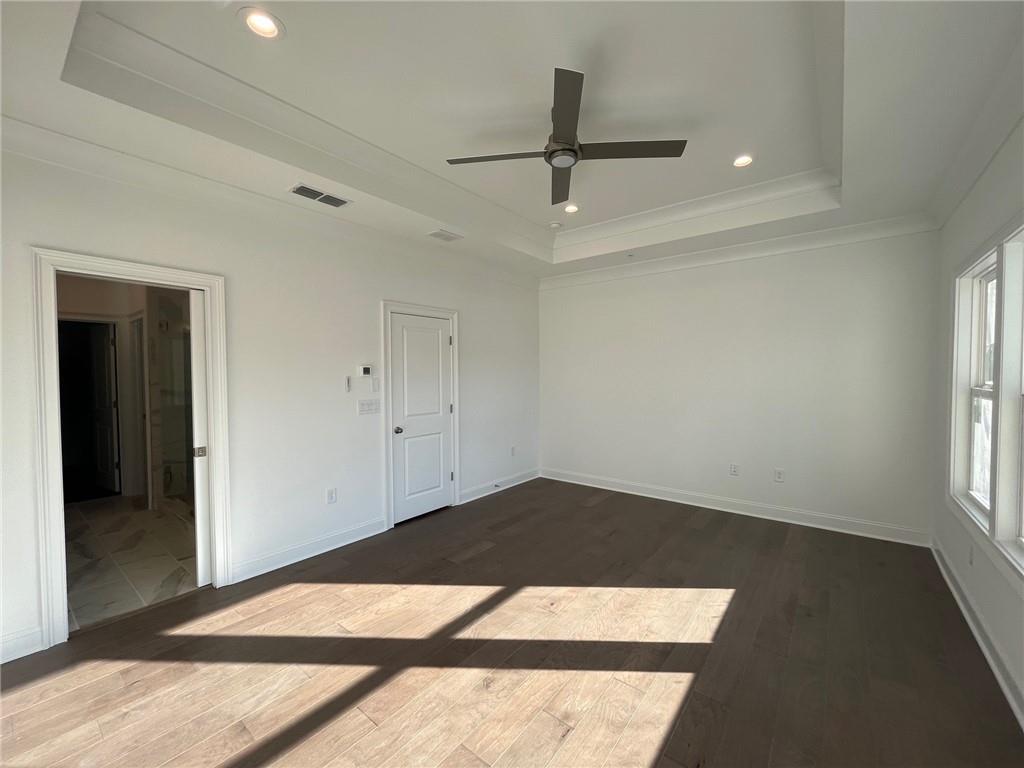 Spare room with a tray ceiling, dark wood-type flooring, and ceiling fan