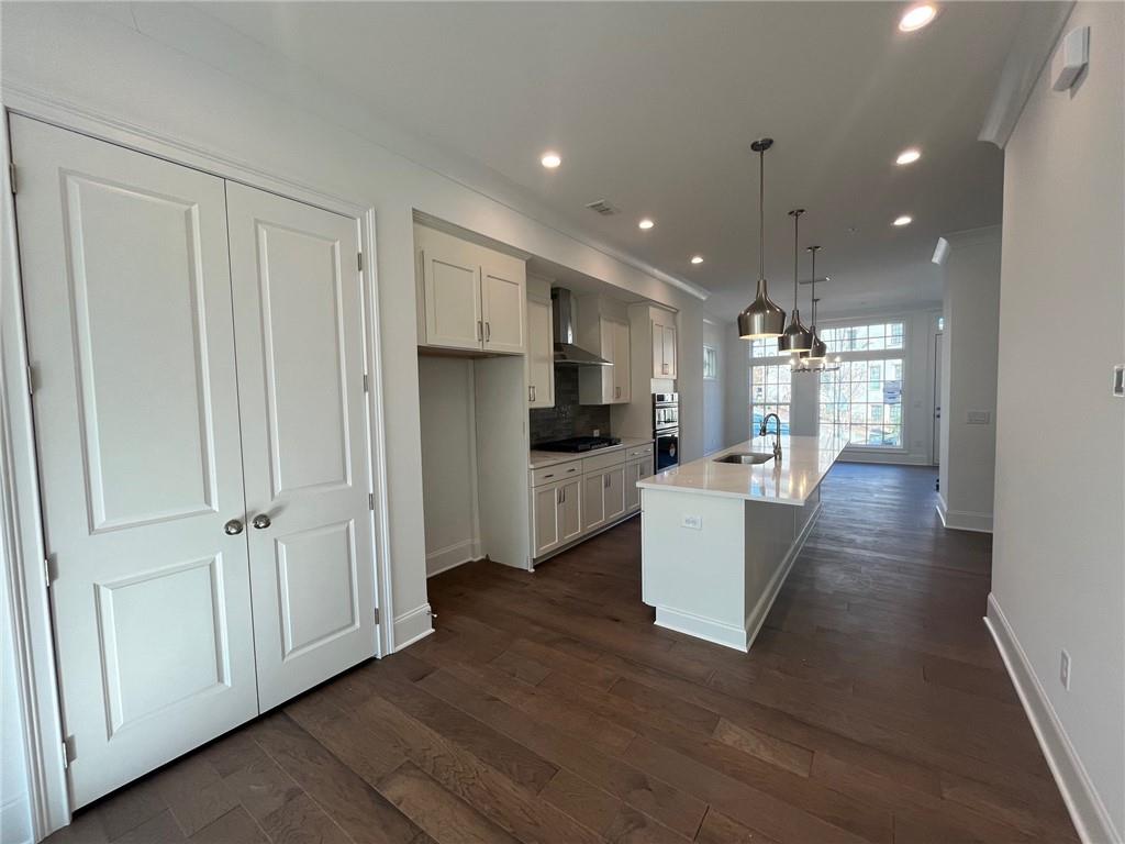Kitchen with wall chimney range hood, pendant lighting, an island with sink, sink, and dark hardwood / wood-style floors