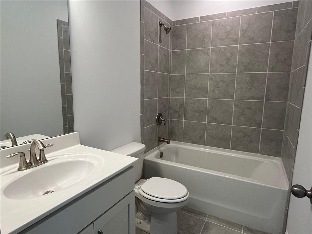 Full bathroom featuring tiled shower / bath combo, toilet, tile flooring, and vanity