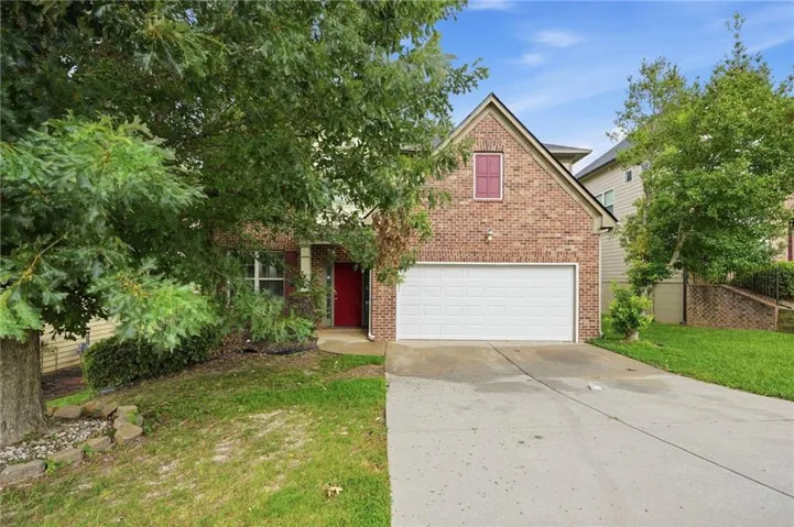 Brick facade home featuring a prominent two-car garage, a vibrant red front door, and a covered porch entry