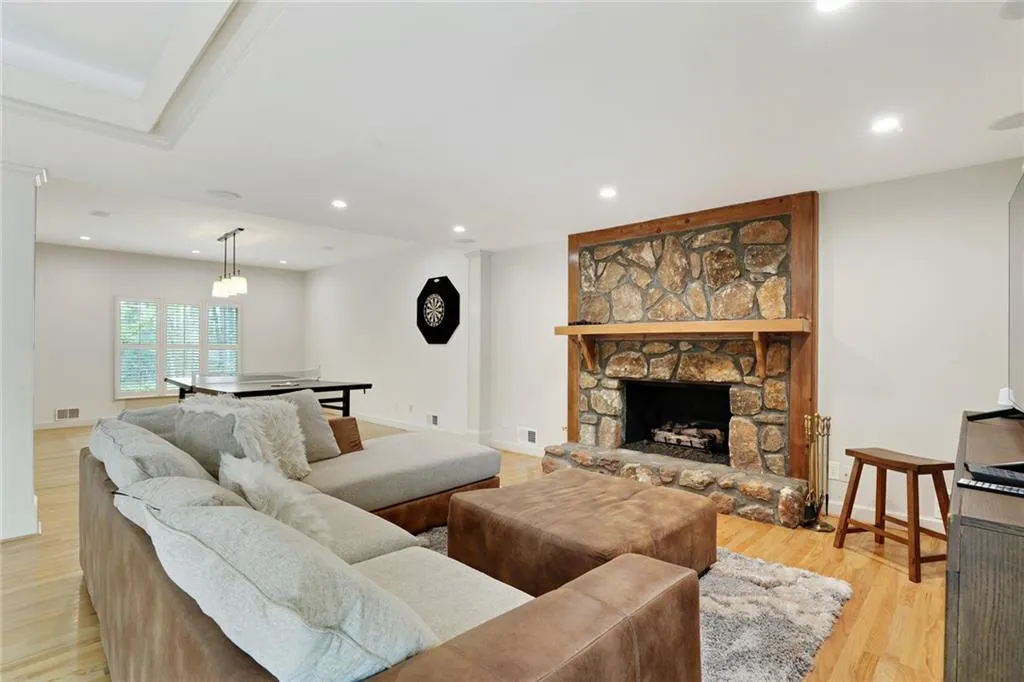 Lower Level--Living room with a stone fireplace and light wood-type flooring off game room