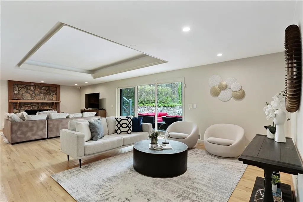 Living room with a stone fireplace, a tray ceiling, and light hardwood / wood-style floors