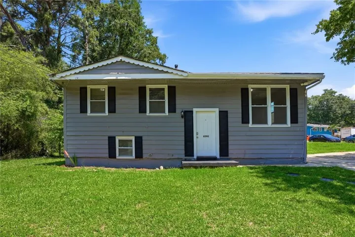 Gray siding exterior featuring a white front door, black shutters, multiple windows, and a green lawn