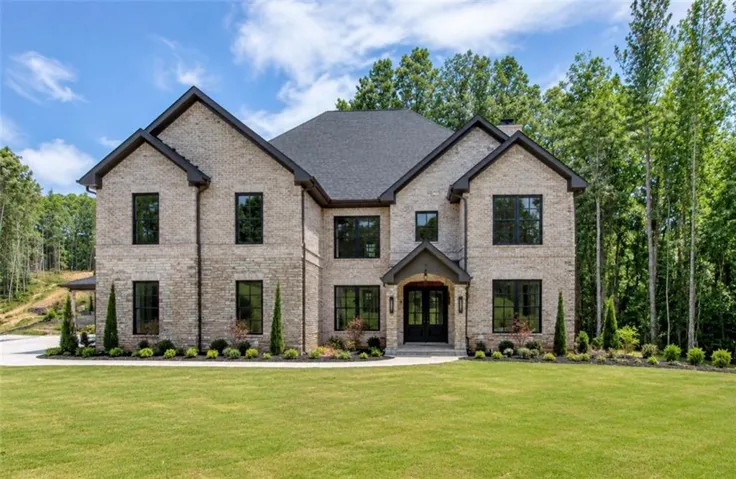 Two-story light-toned brick residence featuring a dark shingle roof and black-framed windows