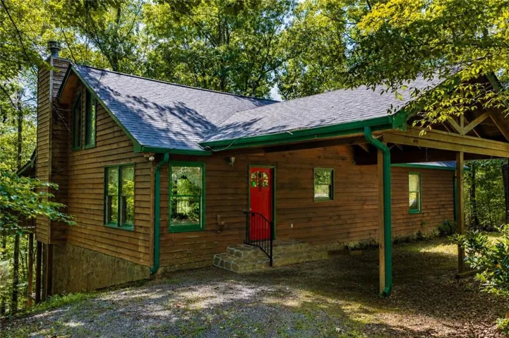 Wood-sided exterior featuring a covered carport, stone chimney, and a vibrant red entry door