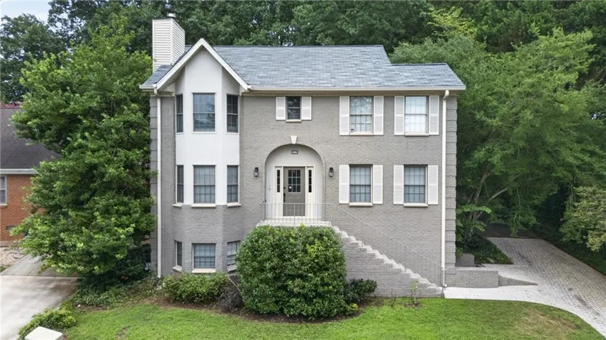 Gray brick exterior with a prominent arched entry, white shutters, a multi-pane front door, a bay window feature, and a paved driveway