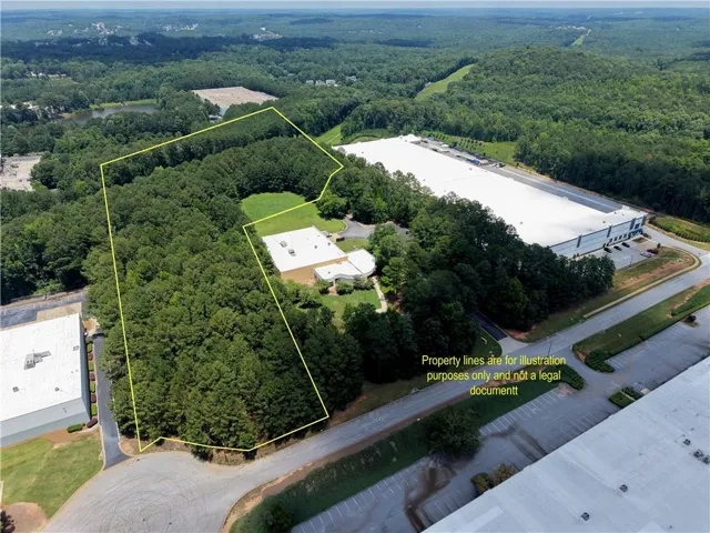 Expansive wooded lot featuring established trees, two existing structures with white roofs, and paved road access