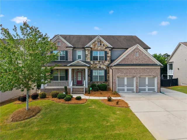 Two-story residence featuring a brick and stone facade, a covered front porch, and a two-car garage with carriage-style doors
