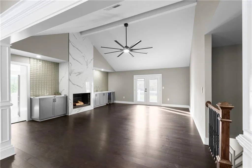 Unfurnished living room with a fireplace, high vaulted ceiling, dark wood finished floors, beamed ceiling, and a ceiling fan