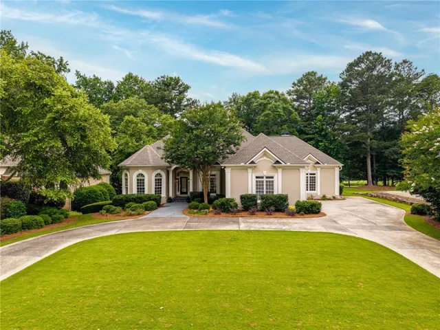 Stucco exterior featuring arched windows, a circular driveway, mature landscaping, a covered entry, and a prominent front lawn