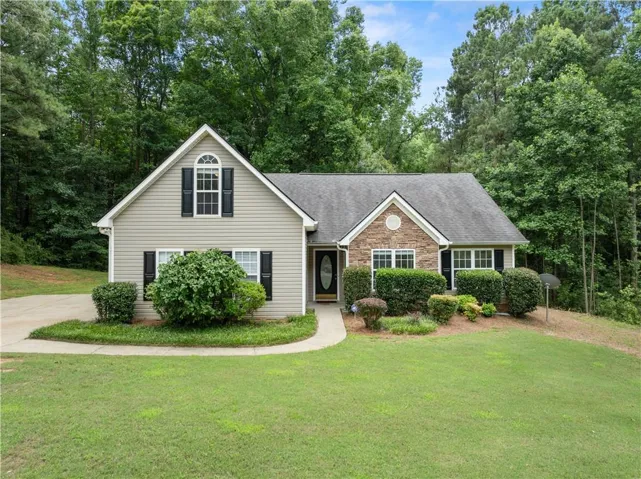 Traditional residence featuring a stone and siding exterior, a front-facing gable with an arched window, a dark gray shingle roof, a concrete driveway, and established front landscaping