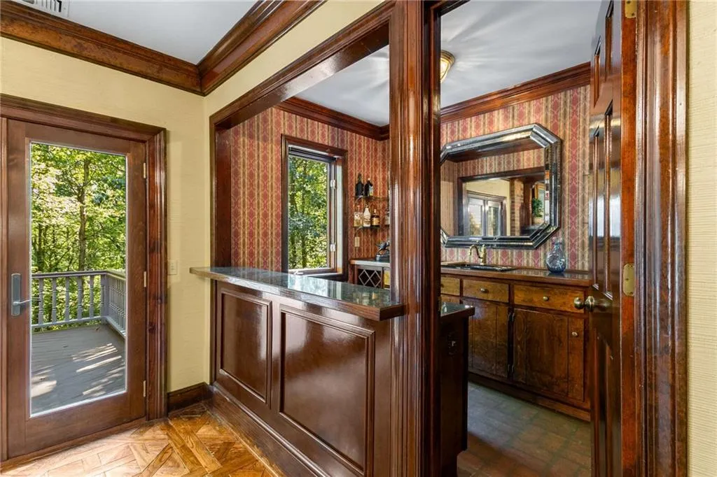 Oversized wet bar with dark stained wood cabinetry and long countertop with shelving and a sink.