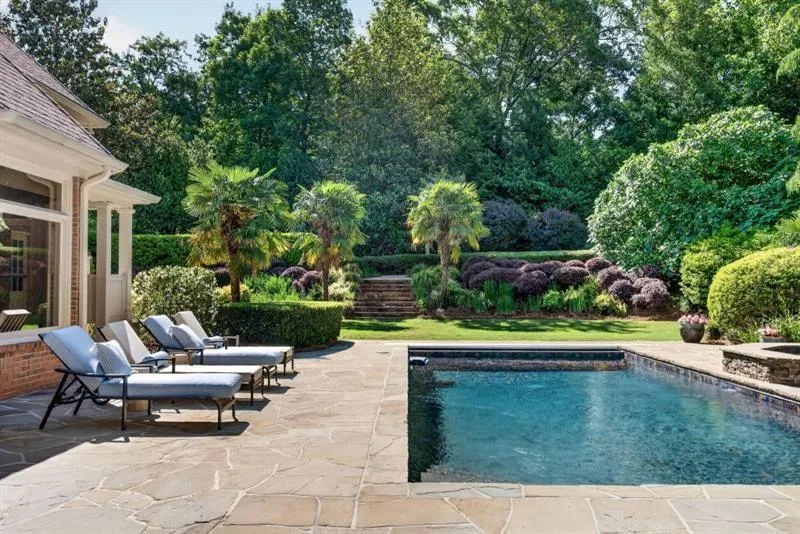 Outdoor pool area featuring a rectangular swimming pool, natural stone patio, and mature landscaping