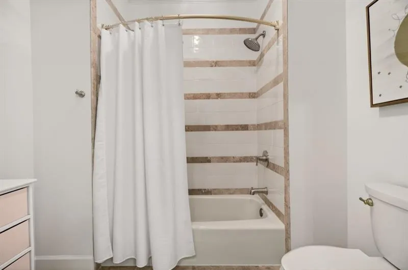Tub and shower combination featuring white subway tile with horizontal accent bands, a polished chrome shower head, and a curved shower curtain rod