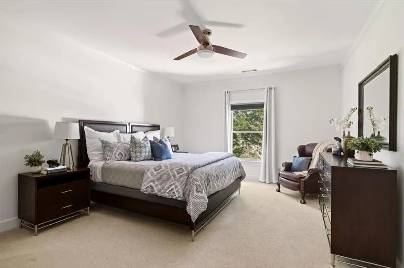 Bright room with neutral carpeting, a ceiling fan, crown molding, and a window with white curtains