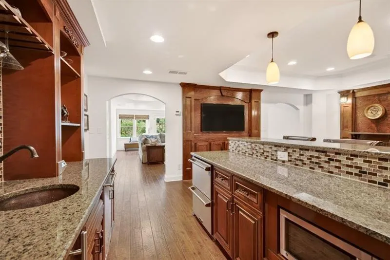 Wet bar featuring granite countertops, a copper sink, built-in shelving, and wood-finish flooring