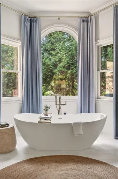 Freestanding soaking tub with a floor-mounted brushed nickel faucet, set against an arched window